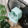 A light blue portable ice-cooling fan is shown in close-up against a blurred green plant background.