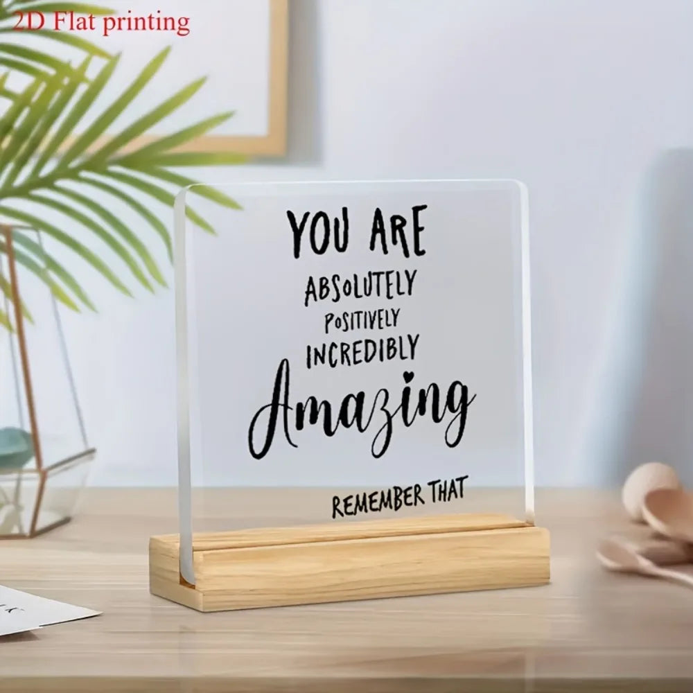 A clear acrylic desktop sign with black script text that reads You are absolutely positively incredibly amazing