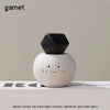 A black bean-shaped garnet crystal resting on a white, smiling stone against a neutral background.