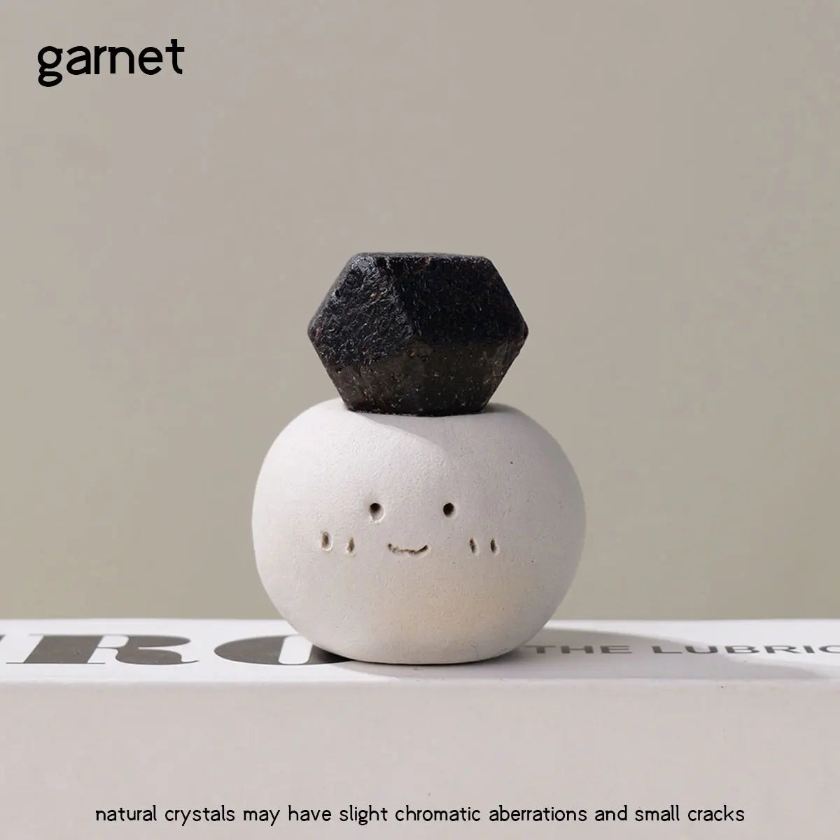 A black bean-shaped garnet crystal resting on a white, smiling stone against a neutral background.