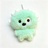 A light green fluffy plush keychain shaped like a monster with white horns and black eyes.