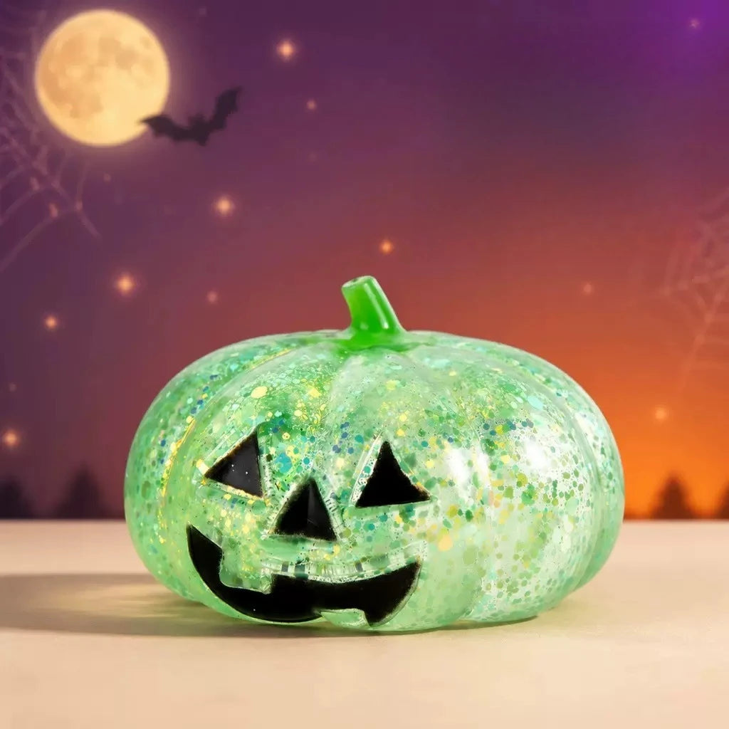 A glowing green Halloween pumpkin stress ball with a carved face sits on a white surface against a purple and orange backgrou