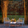 Outdoor scene featuring a string of warm LED curtain lights hanging between two white wooden benches.