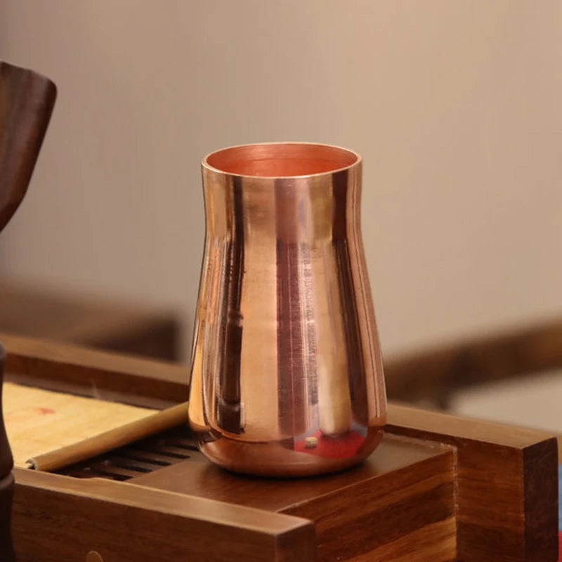 A handcrafted pure copper vintage mug with a tapered shape rests on a wooden surface.