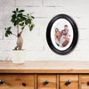 A classic solid wood oval picture frame with a light interior is displayed on a wooden cabinet top next to a potted green pla