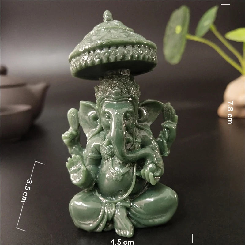 A small, green bronze Ganesha Buddha statue with a tiered crown sitting on a dark surface.
