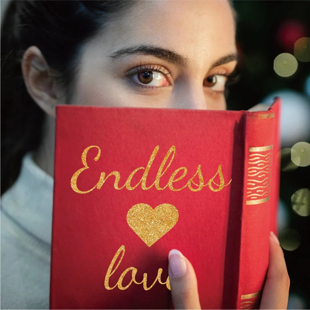 A close-up of a person holding a red book with gold lettering, featuring an endless love design.