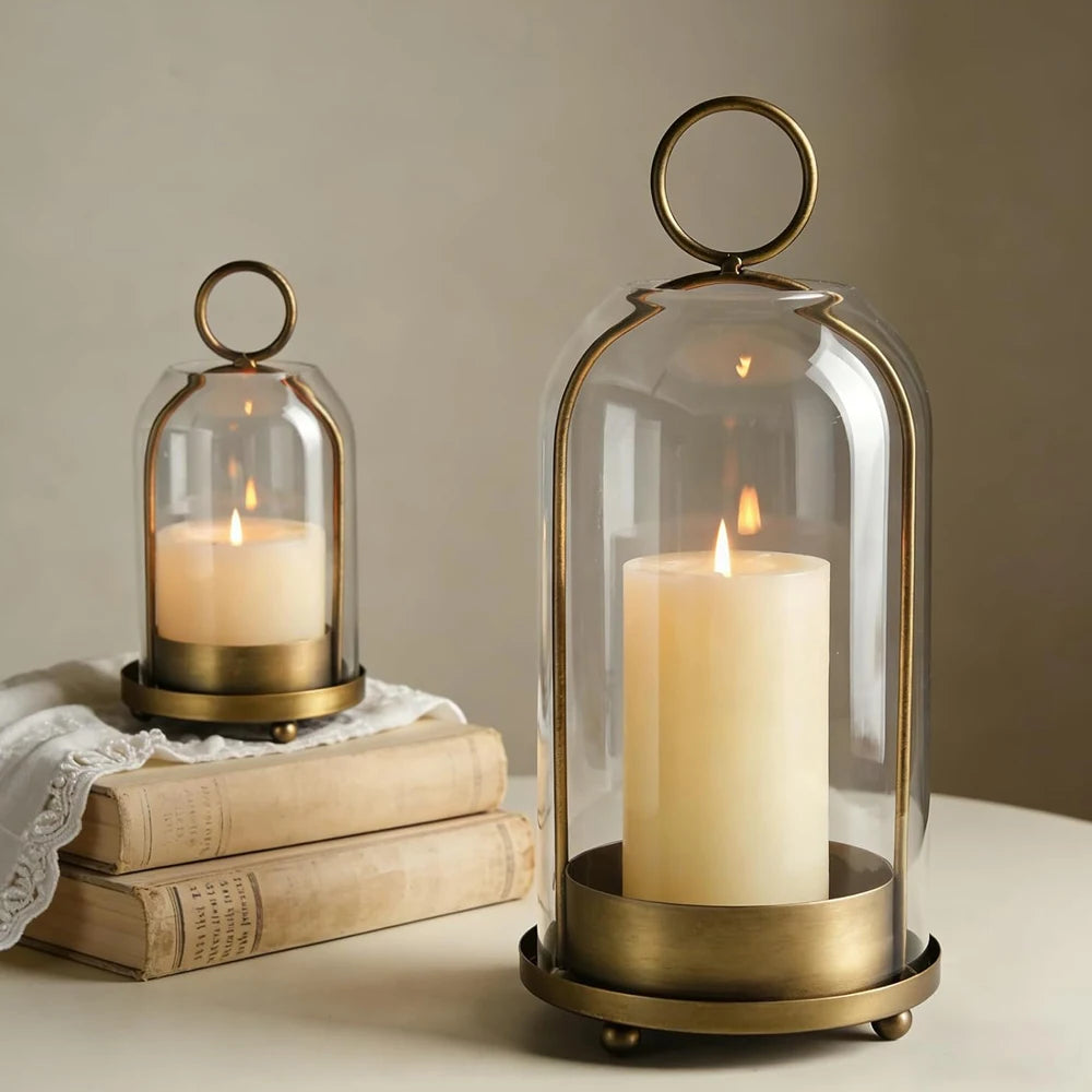 Antique brass metal candle holders with glass domes displaying glowing candles on a wooden surface.