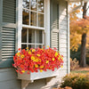 A vibrant bouquet of artificial pansy flowers in shades of orange and yellow sits in a white planter next to a window.