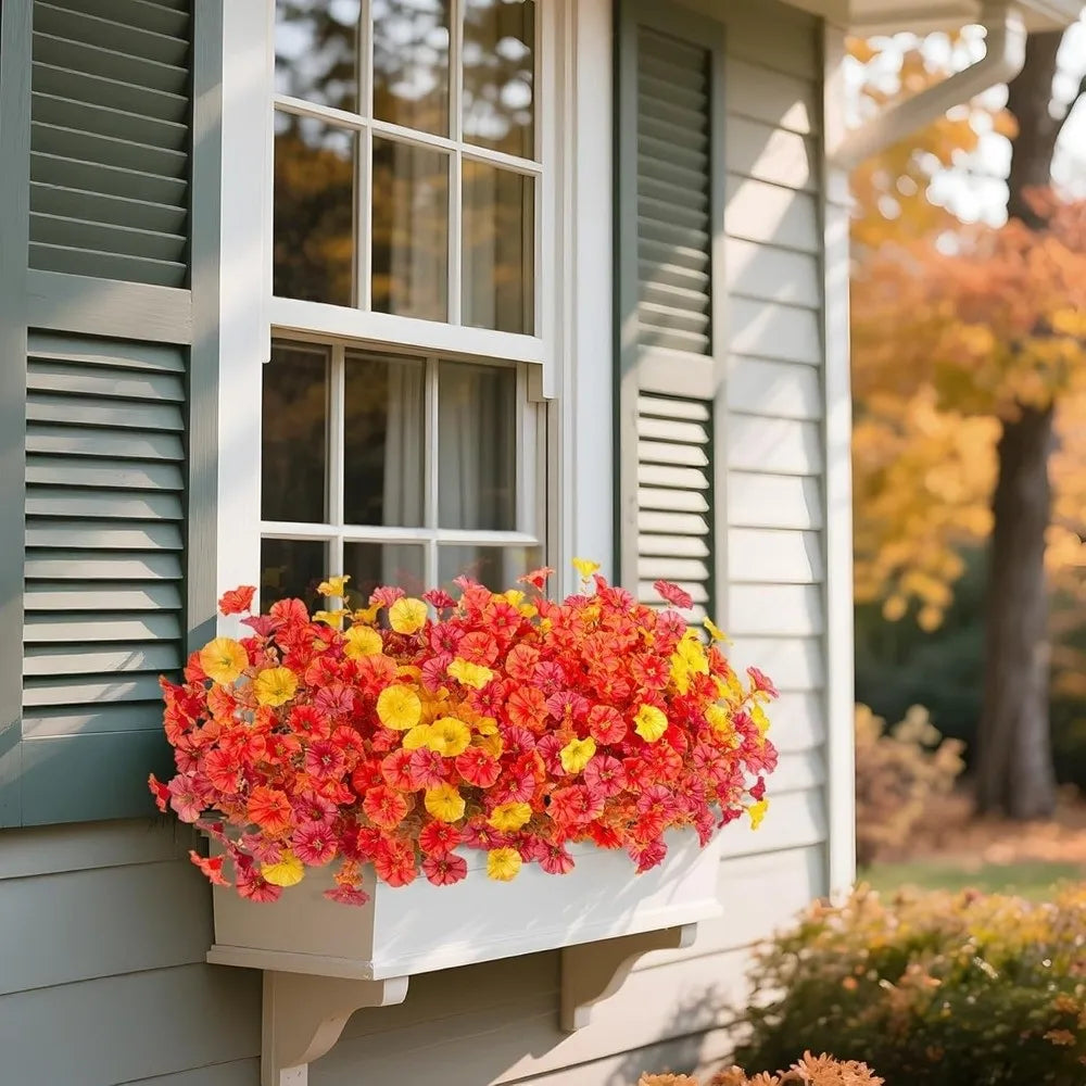 A vibrant bouquet of artificial pansy flowers in shades of orange and yellow sits in a white planter next to a window.
