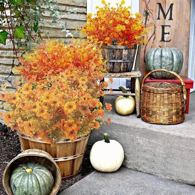 An artificial fall flower bouquet featuring orange and yellow foliage displayed in a wooden planter next to a decorative pump