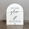 A white acrylic sign with black script that reads Let Love glow and instructs to grab a glow stick and light up the dance flo