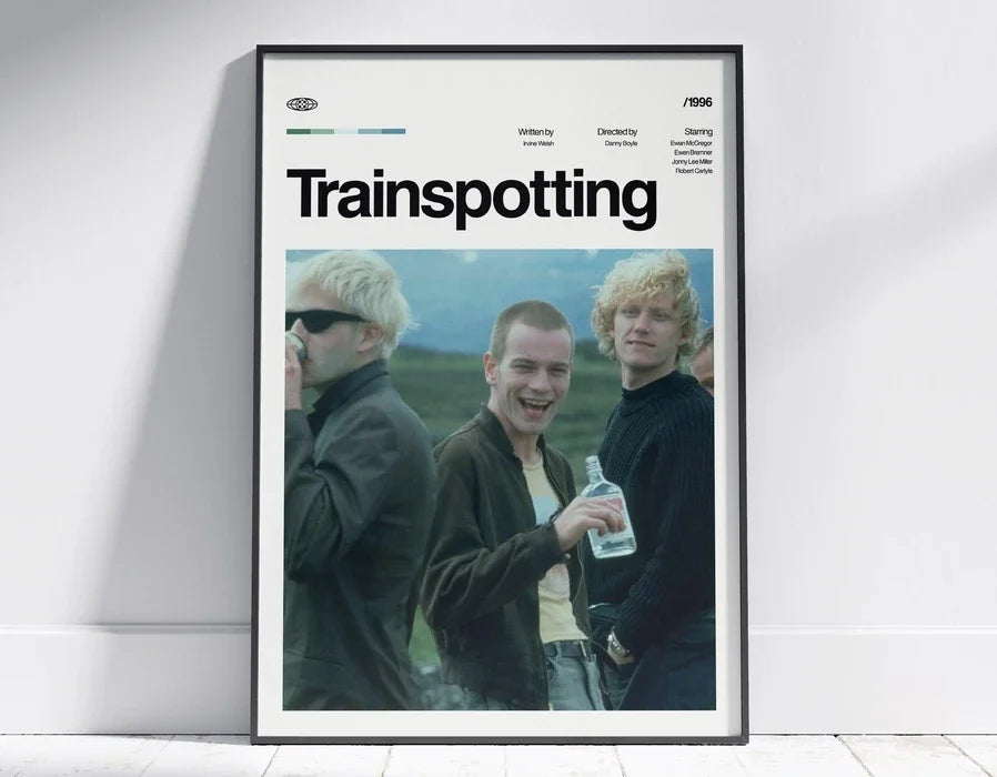 A framed poster titled Trainspotting featuring three men in dark clothing and a light-colored background.