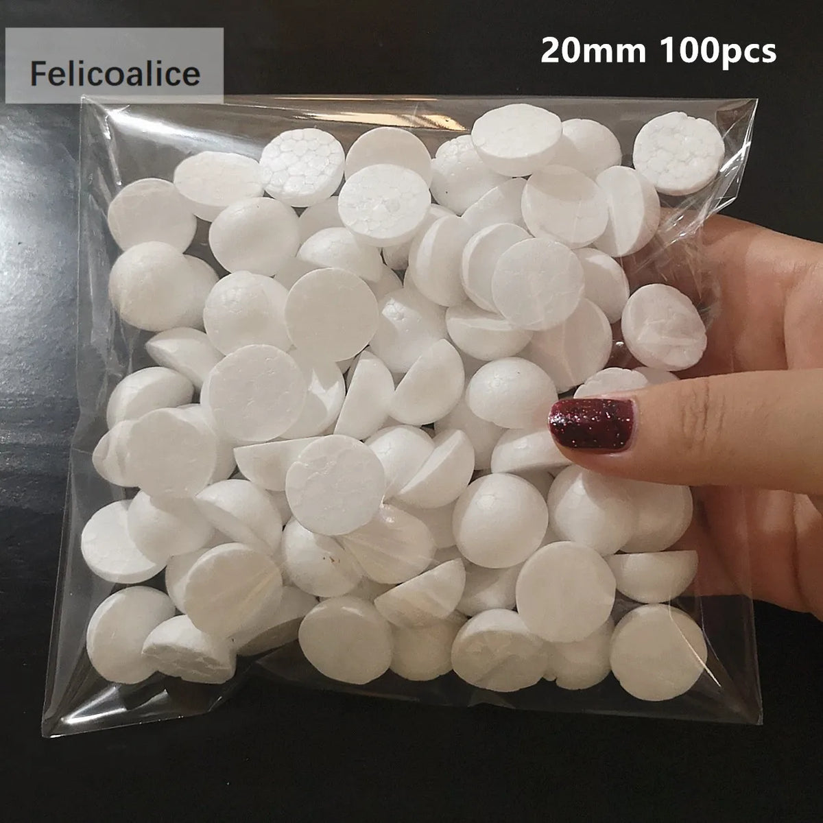 A hand holds a clear plastic bag filled with 100 white polystyrene foam balls, 20mm in diameter.