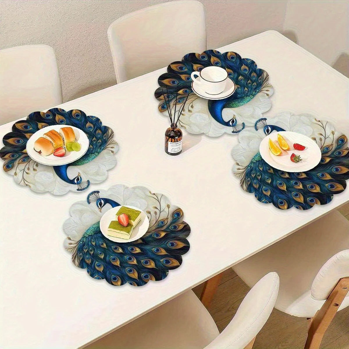 A set of four elegant peacock feather placemats is displayed on a white dining table with food and a teacup.
