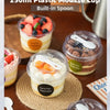 A clear plastic mousse cup with a built-in spoon filled with a creamy dessert on a woven mat.