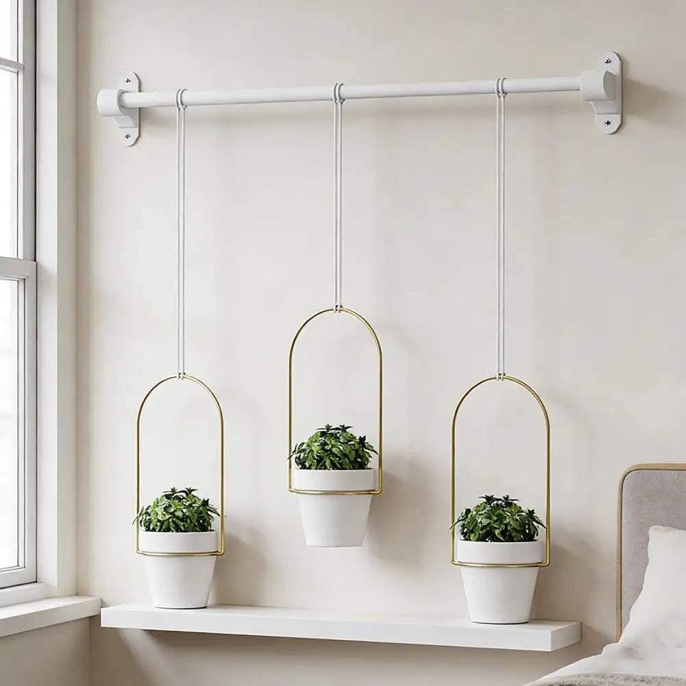 Ein Set aus drei goldfarbenen Hängepflanztopfhaltern an einer weißen Wand.