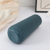 A teal plastic cylindrical vase with vertical ridges is shown on a white surface next to a cream fabric.