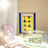A vibrant acrylic photo frame displaying a yellow mosaic and a clear glass frame with a green patterned message board.