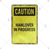 A yellow vintage tin sign with black text warning of a hangover in progress.