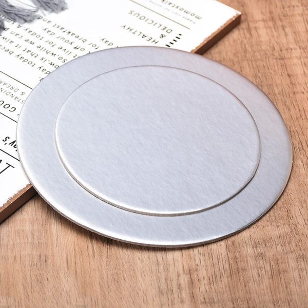 A round silver coated cake board resting on a wooden surface next to a piece of paper.