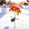 A solar-powered poinsettia garden light with bright red flowers growing in a snowy outdoor setting.
