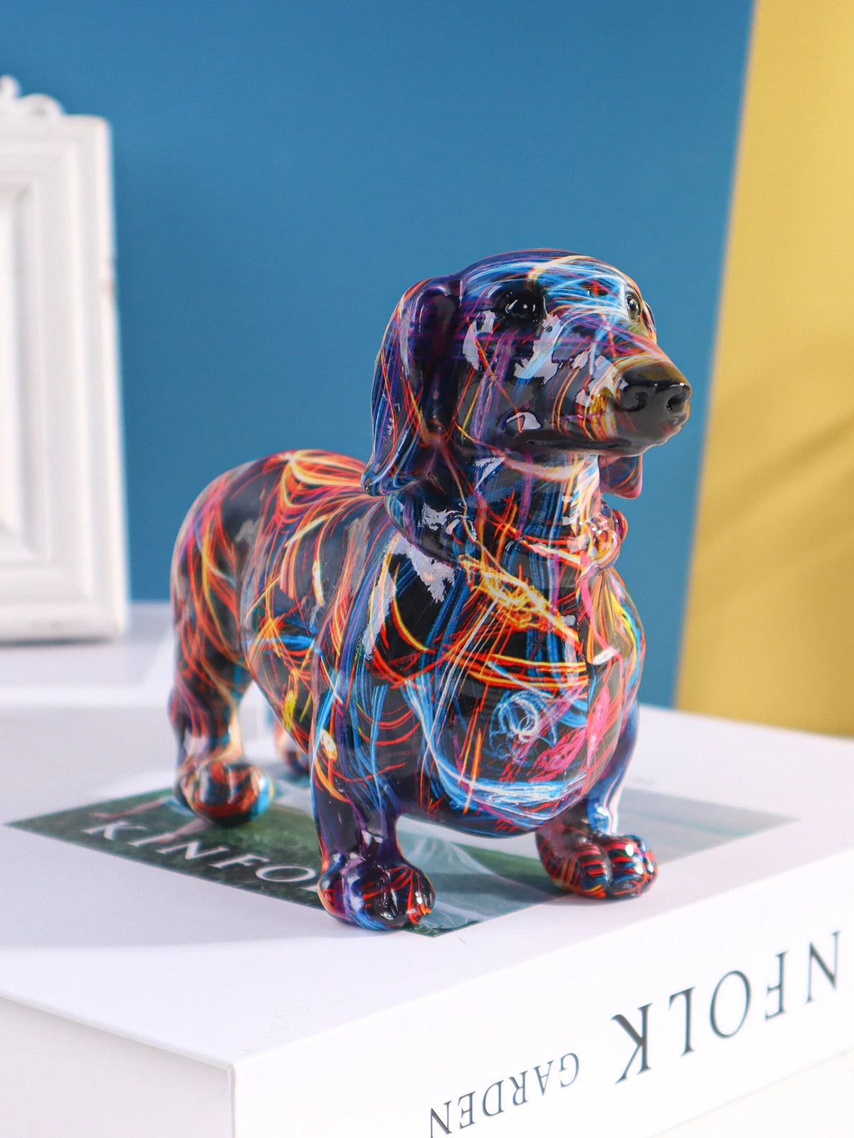 A colorful resin figurine of a dachshund dog standing on a white box.