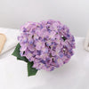 A cluster of purple artificial hydrangea flowers resting on a white surface.