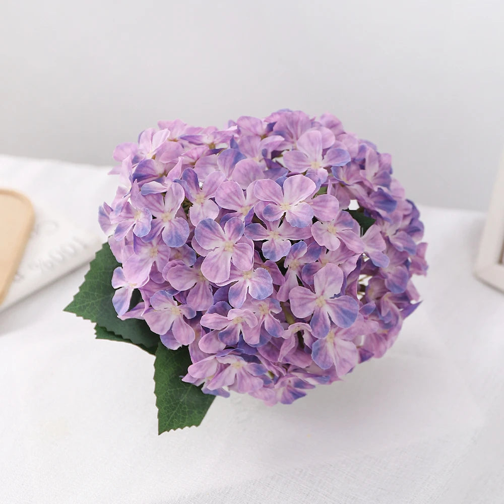 A cluster of purple artificial hydrangea flowers resting on a white surface.