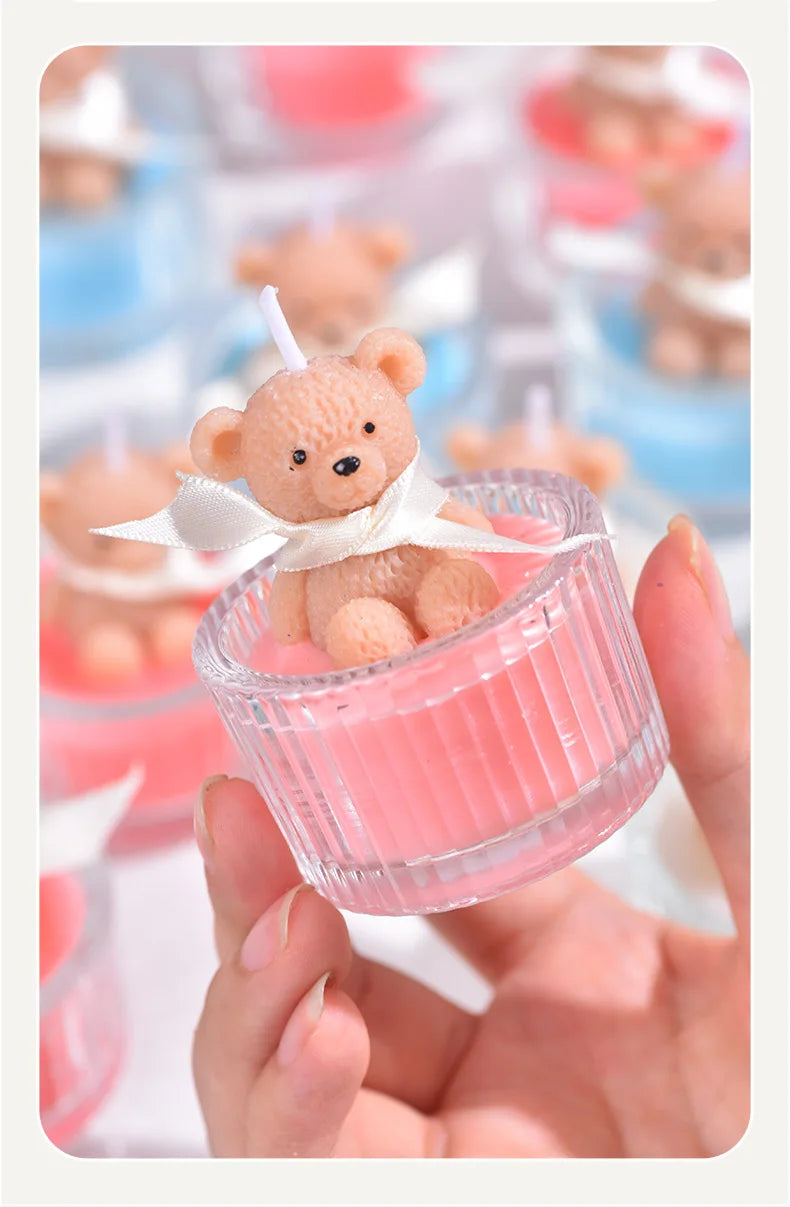 A small teddy bear candle in a pink glass jar with a white ribbon being held by a hand.