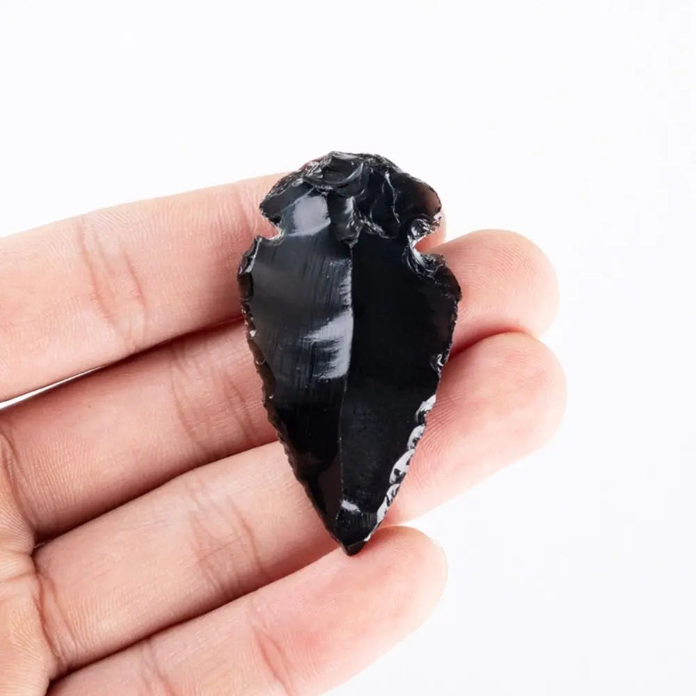 A hand holds a polished, black obsidian arrow pendant crystal charm.