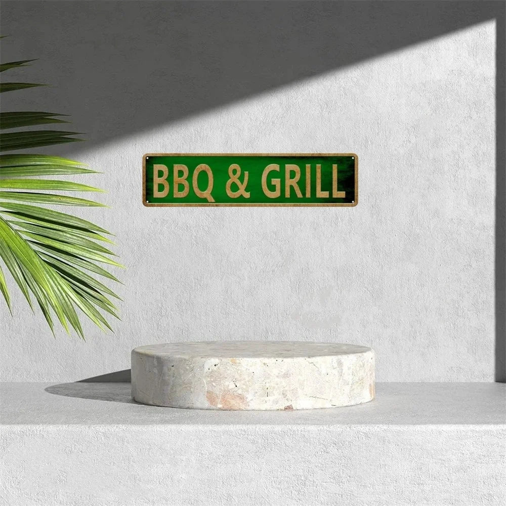 A green metal tin sign with BBQ & GRILL text mounted on a gray wall above a light stone slab.