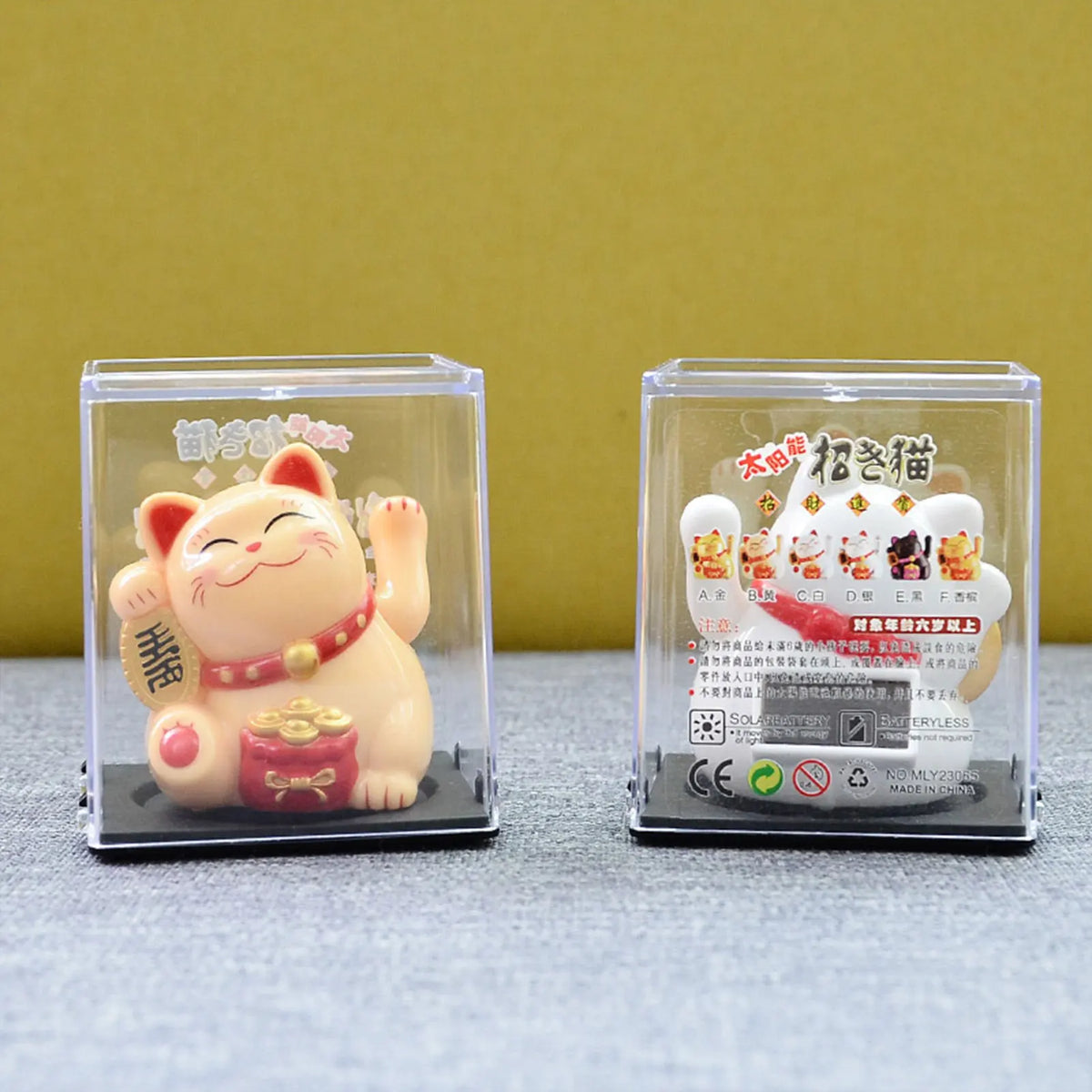 A solar-powered figurine of a pink cat with a red collar and gold accessories displayed in a clear plastic case.