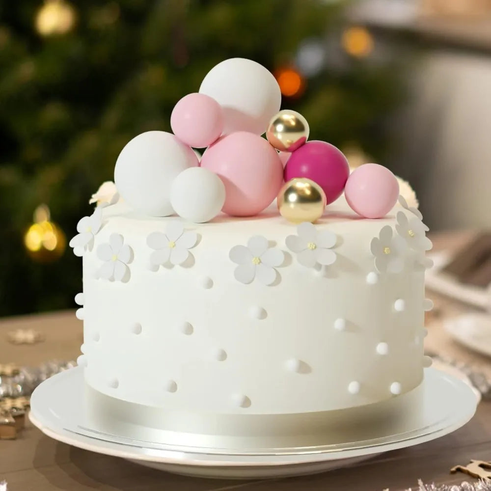 White cake decorated with pink and gold foam ball toppers on a silver platter.