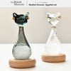 A glass bottle shaped like an Egyptian cat with a green body and gold accents, displayed on a wooden base.