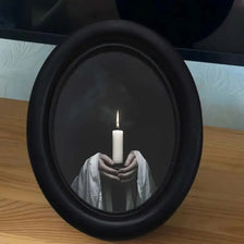 A black framed candle holder displays a lit white candle held by hands wrapped in white fabric.