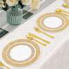 A set of elegant gold rim plastic dinner and dessert plates arranged on a white tablecloth with cutlery and floral decor.