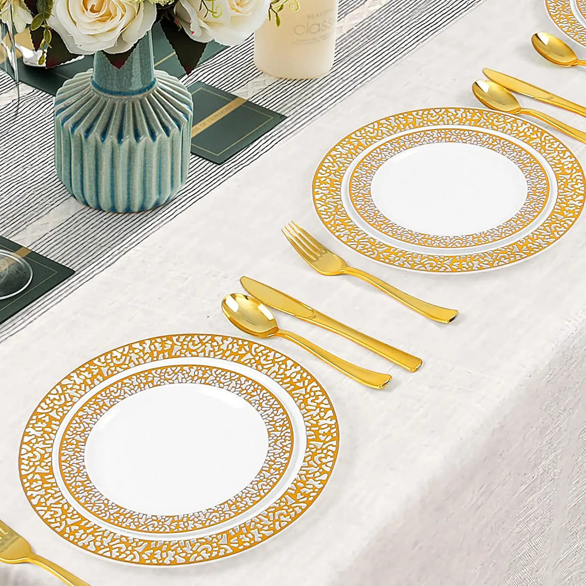 A set of elegant gold rim plastic dinner and dessert plates arranged on a white tablecloth with cutlery and floral decor.