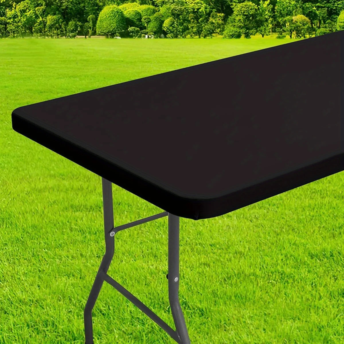 A black stretchy waterproof table cover is shown on a folding table outdoors on green grass.