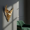 Ornate winged heart wall decor in gold metal mounted on a gray wall.