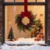 An artificial Christmas wreath with green foliage, red berries, and a large red velvet bow displayed in a window.