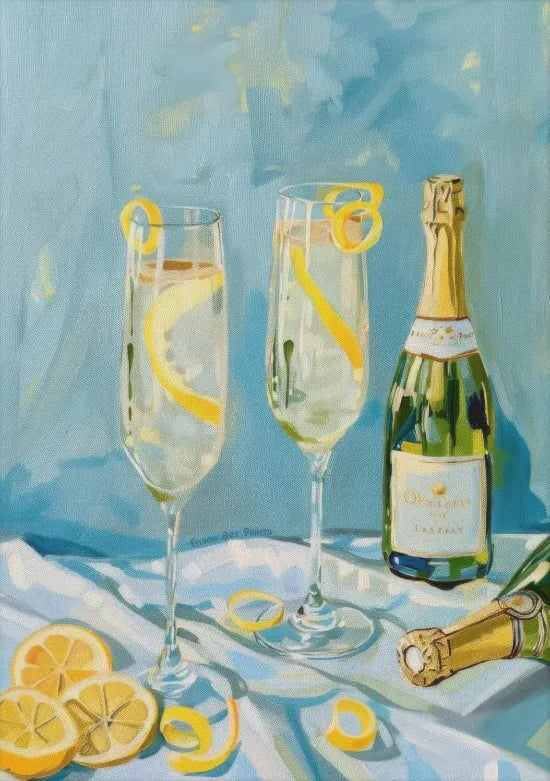 A glass of sparkling wine and lemon slices are displayed on a white cloth with a bottle in the background.