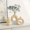 A set of organic ceramic vases in beige and cream colors with a sprig of greenery on a white shelf.