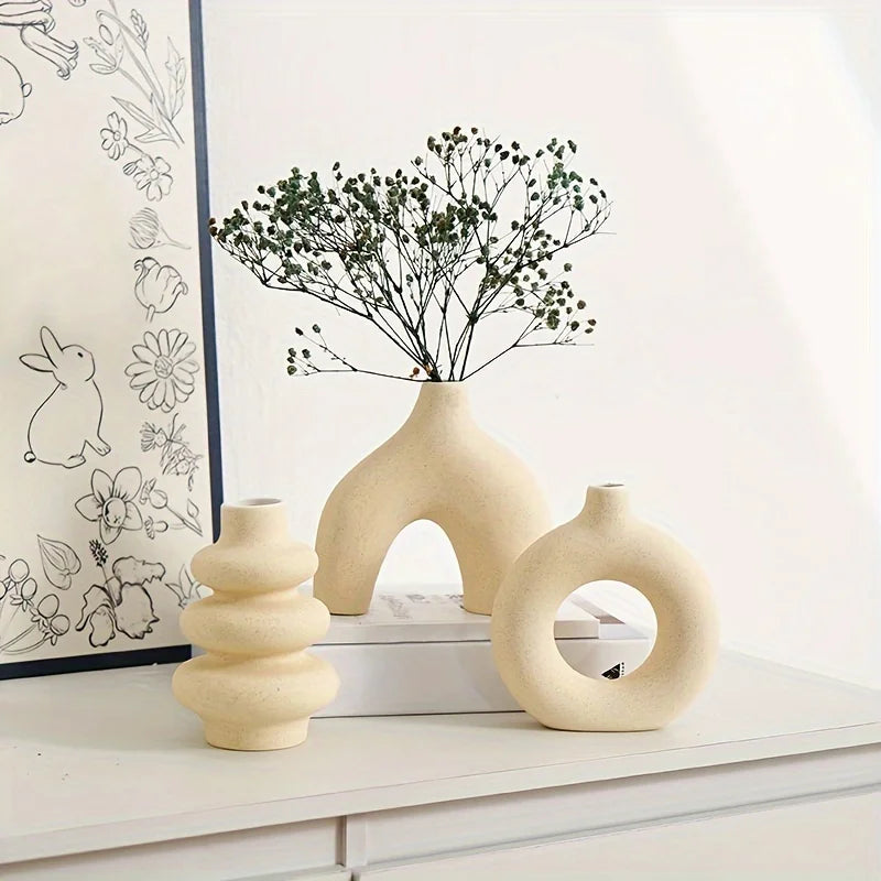 A set of organic ceramic vases in beige and cream colors with a sprig of greenery on a white shelf.