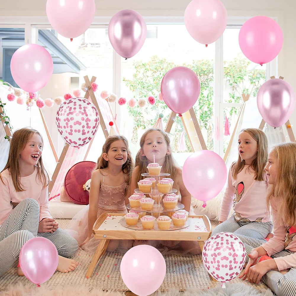 Six children sitting on the floor surrounded by pastel pink and white latex balloons with metallic confetti accents