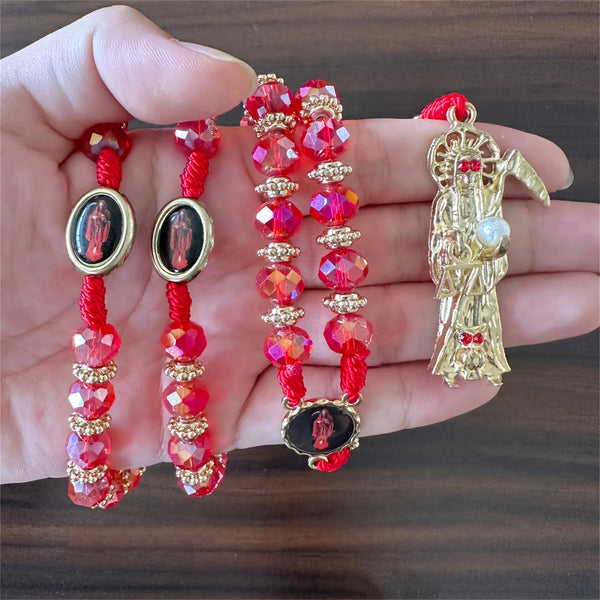 A hand holds a rosary necklace featuring red and pink beads, gold accents, and a figure of Santa Muerte.