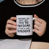 A person holds a white ceramic coffee mug with black text that reads Sometimes you forget that you're awesome so this is your