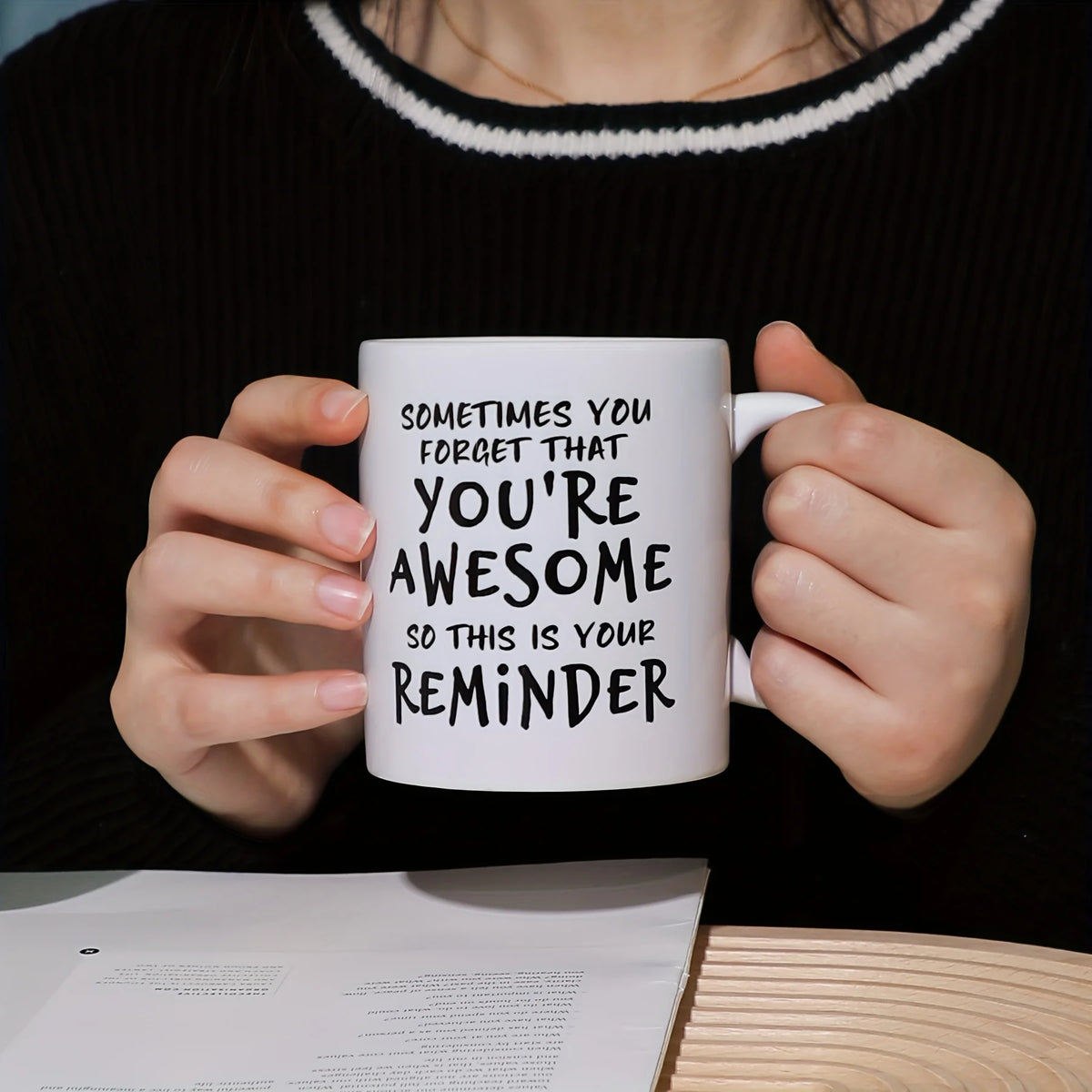 A person holds a white ceramic coffee mug with black text that reads Sometimes you forget that you're awesome so this is your