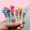 A hand holds a set of five cute cartoon mini ballpoint pens featuring characters like a pink dinosaur, a green avocado, and a