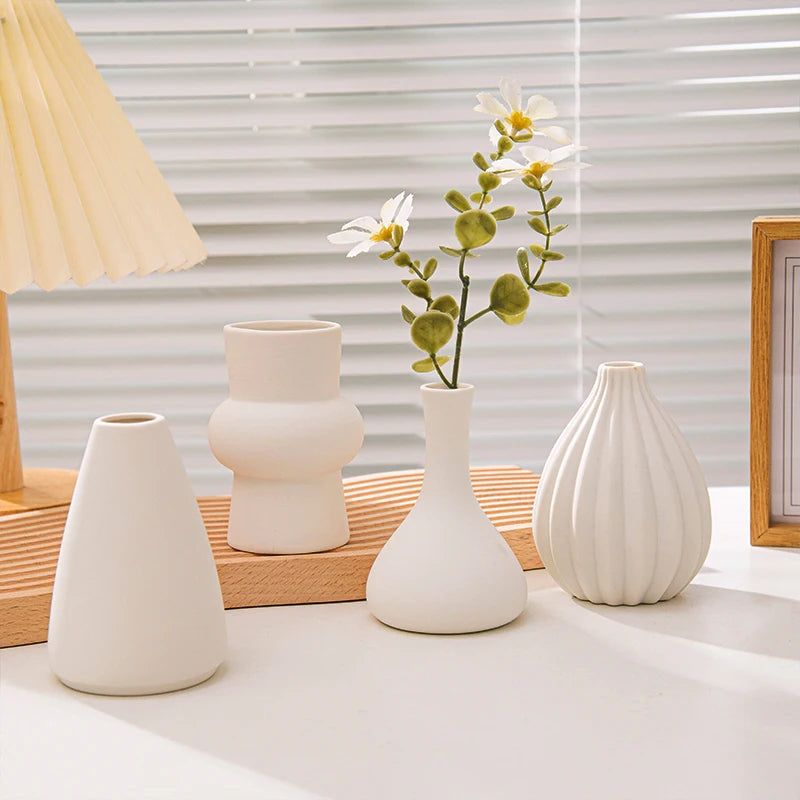 A collection of white ceramic vases and a plant arrangement displayed on a wooden surface next to a window.